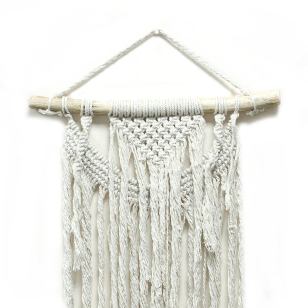 White macrame wall hanging with wooden rod on a white background