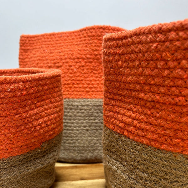 Three woven baskets with orange and brown layers on a wooden surface.