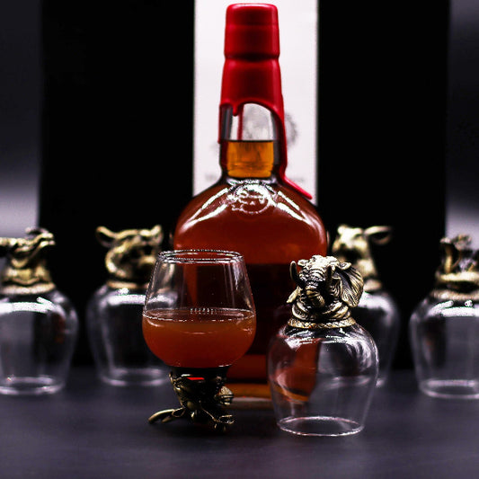 Bottle of whiskey with a red cap and a glass filled with amber liquid on a dark background.