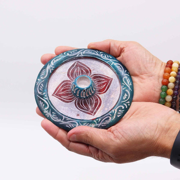 Hand holding a decorative stone with floral design against a white background