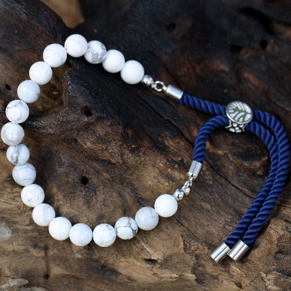 White beaded bracelet with silver clasps and blue braided cord on a wooden surface