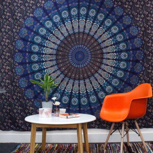 Mandala tapestry on a wall with orange chairs and a small table below.