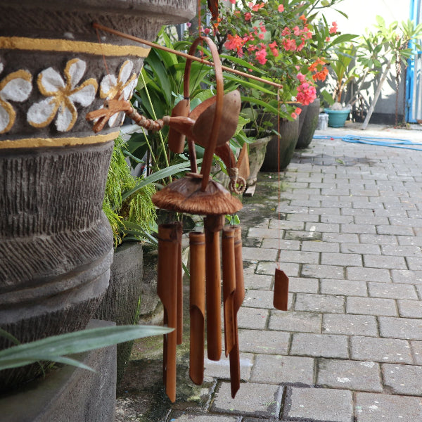 Wooden wind chime in front of decorative pots with floral patterns on a stone path.