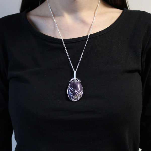 Person wearing a black shirt with a silver necklace featuring a purple pendant.