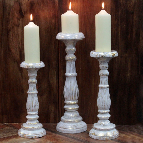 Three white candles in decorative candlesticks against a wooden background