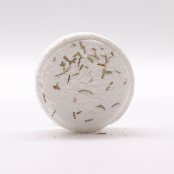 Round white bath bomb with green herbs on a light gray background
