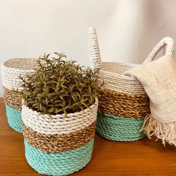 Three woven baskets with a plant and a blanket on a wooden surface