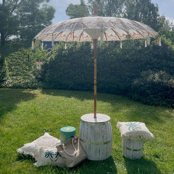 Decorative outdoor umbrella on a wooden barrel with cushions and a bag in a garden setting