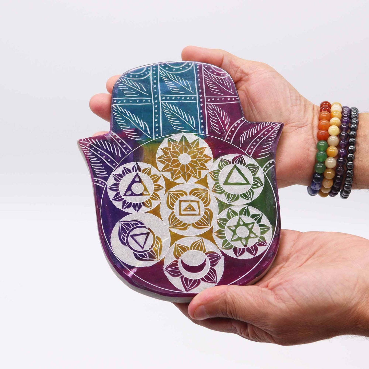 Hand holding a colorful Hamsa-shaped object with geometric patterns on a white background