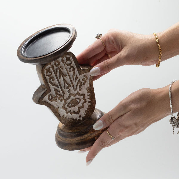 Hand holding a decorative wooden item with intricate carvings on a light background