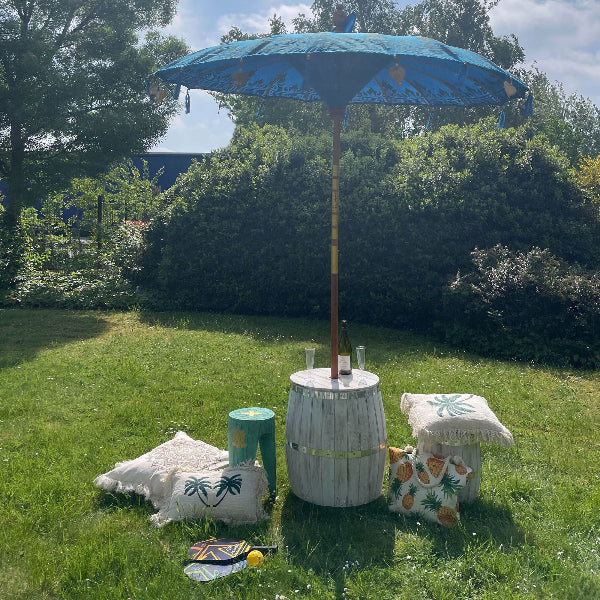 Outdoor setting with a blue umbrella, barrel table, and decorative items on grass