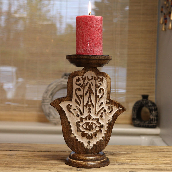 Wooden candle holder with Hamsa design holding a pink candle on a wooden surface.