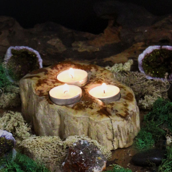 Three lit candles on a wooden stump surrounded by moss and rocks