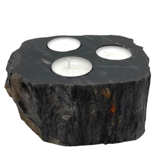 Decorative candle holder made of dark stone with three white candles inside on a white background