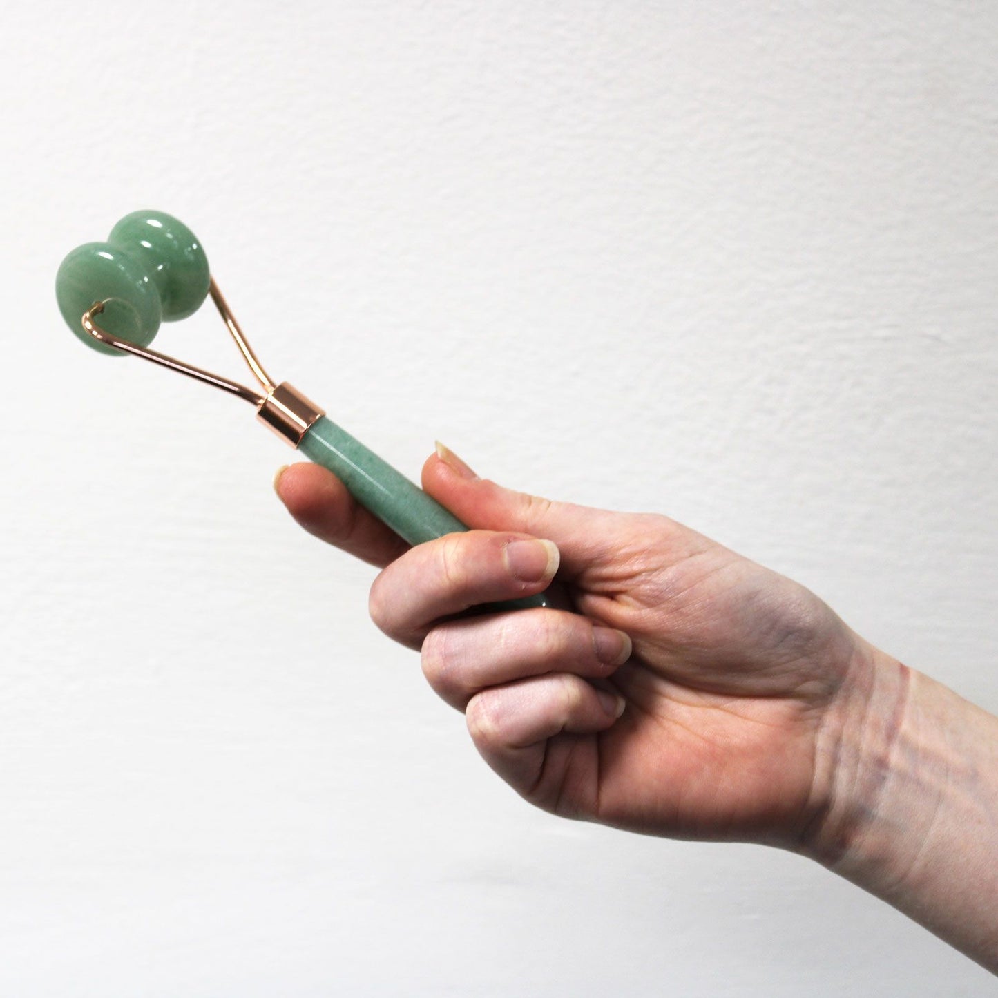 Hand holding a jade roller against a white background