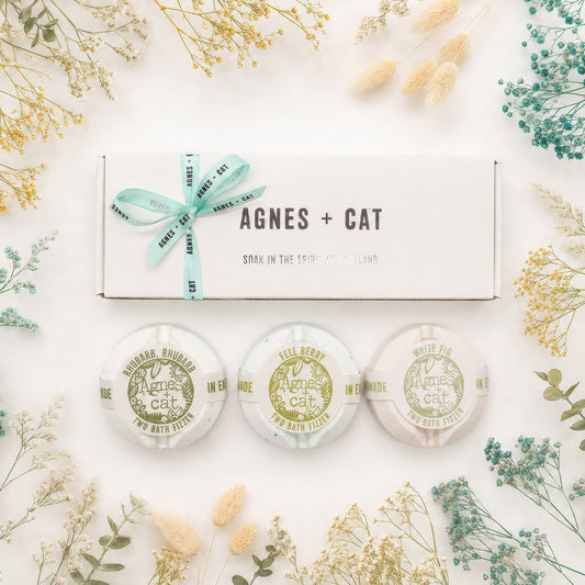 Three bath pillows with 'Agnes + Cat' branding on a white background with decorative plants.
