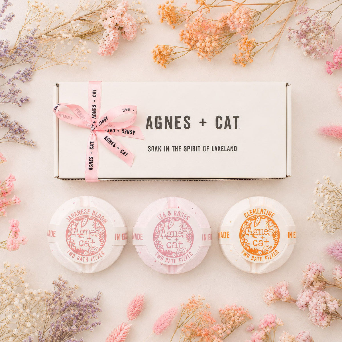 Three bath bombs with 'Agnes + Cat' branding surrounded by dried flowers on a light background.