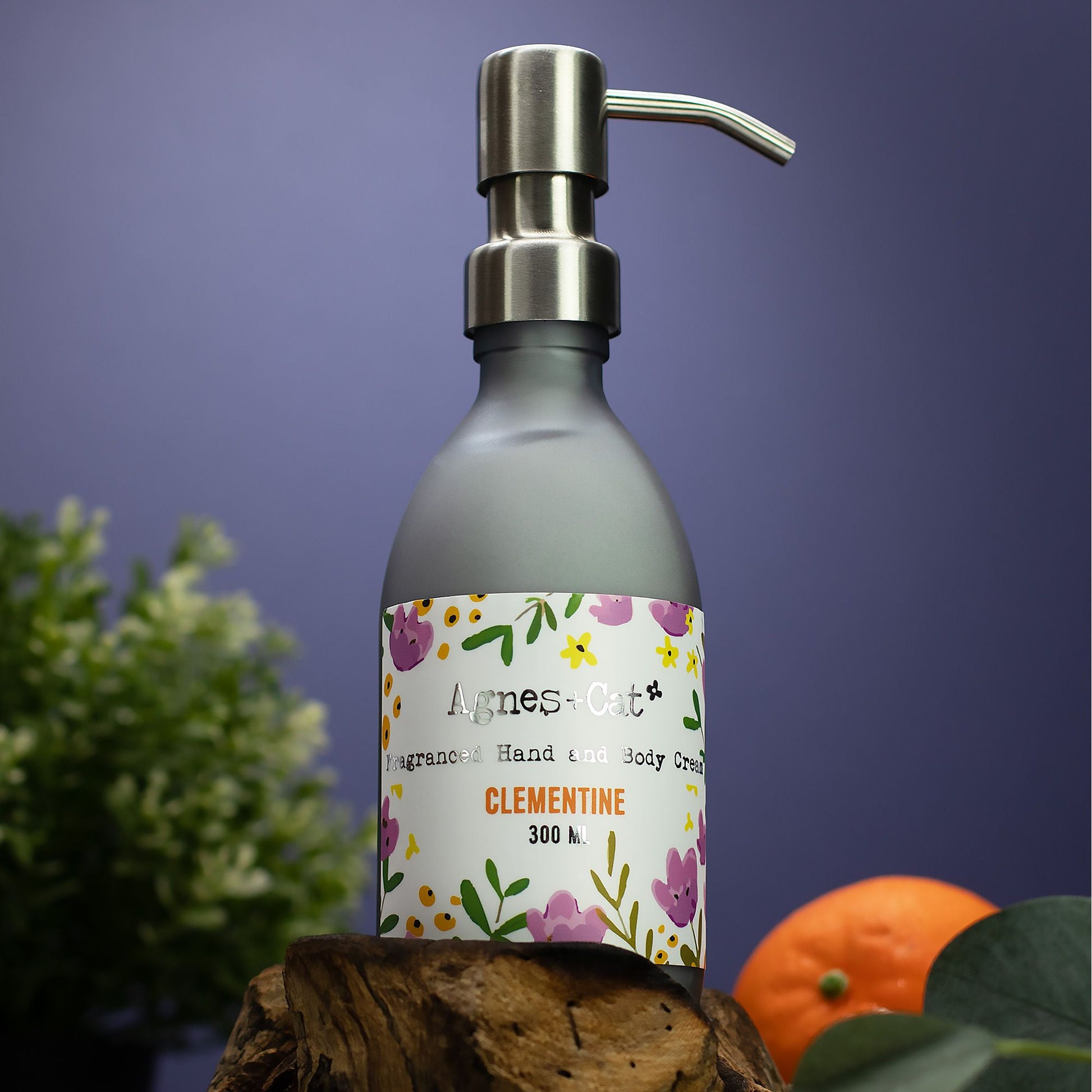Bottle of Agnes & Co Clementine hand cream with a floral label on a wooden surface against a purple background.