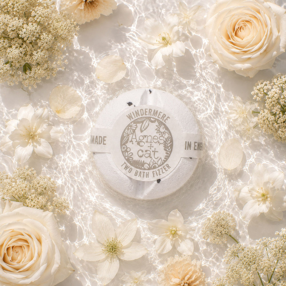 Round bath fizzer with branding surrounded by white flowers on a light background