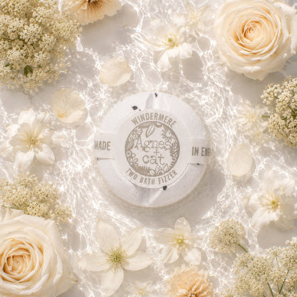 Round bath fizzer with branding surrounded by white flowers on a light background