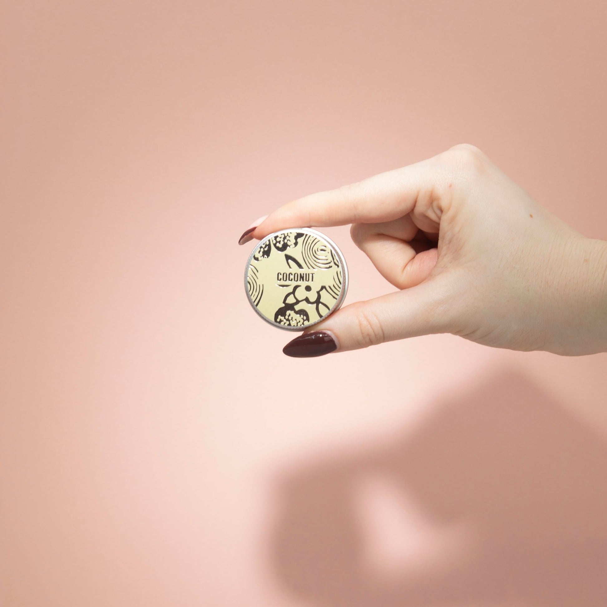 Hand holding a round product with 'Coconut' text against a pink background