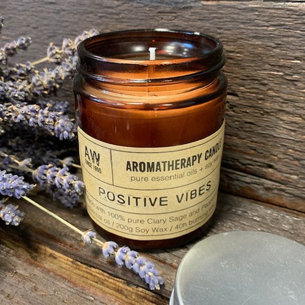 Aromatherapy candle labeled 'Positive Vibes' with lavender flowers on a wooden surface