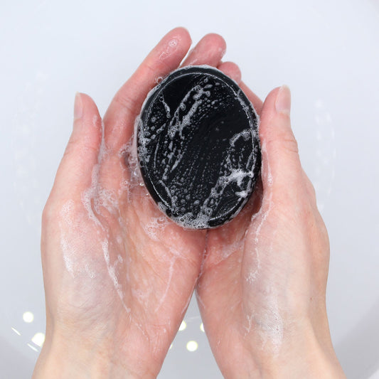 Black cleansing pad with soap suds held between hands against a light background