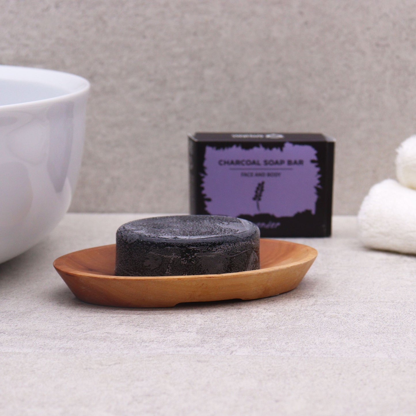 Charcoal soap bar on a wooden dish with a purple box labeled 'Charcoal Soap Bar' in the background.