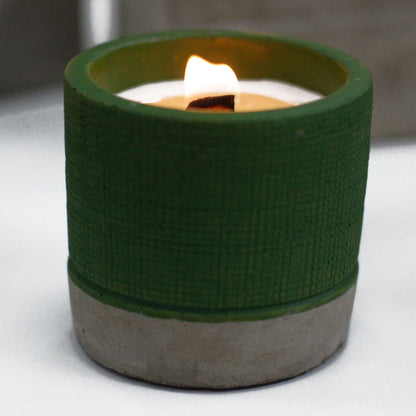 Candle in a green and concrete holder on a white surface