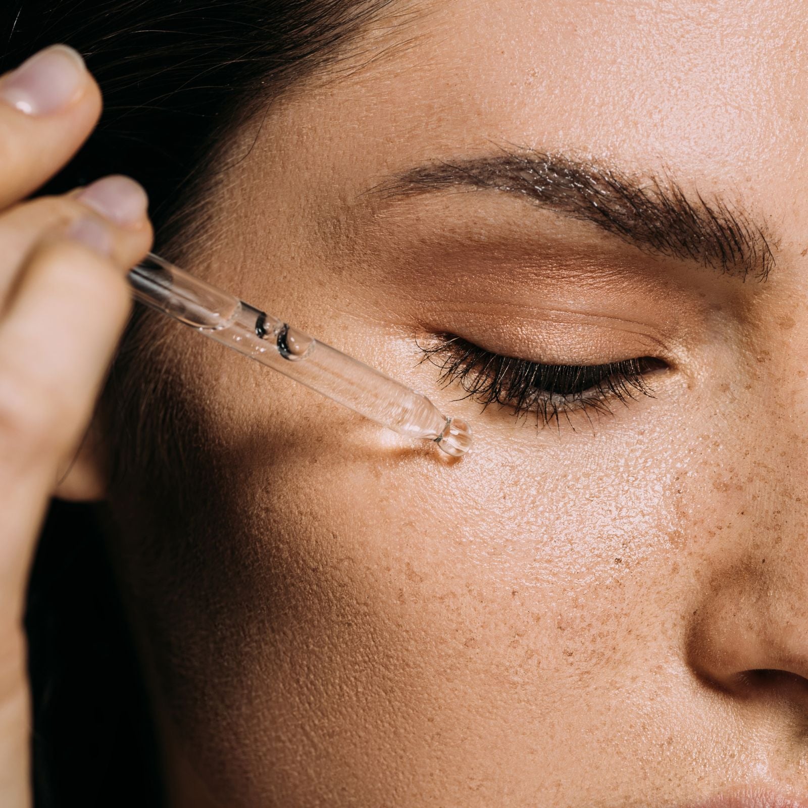 Close-up of a woman applying a dropper to her eye area.