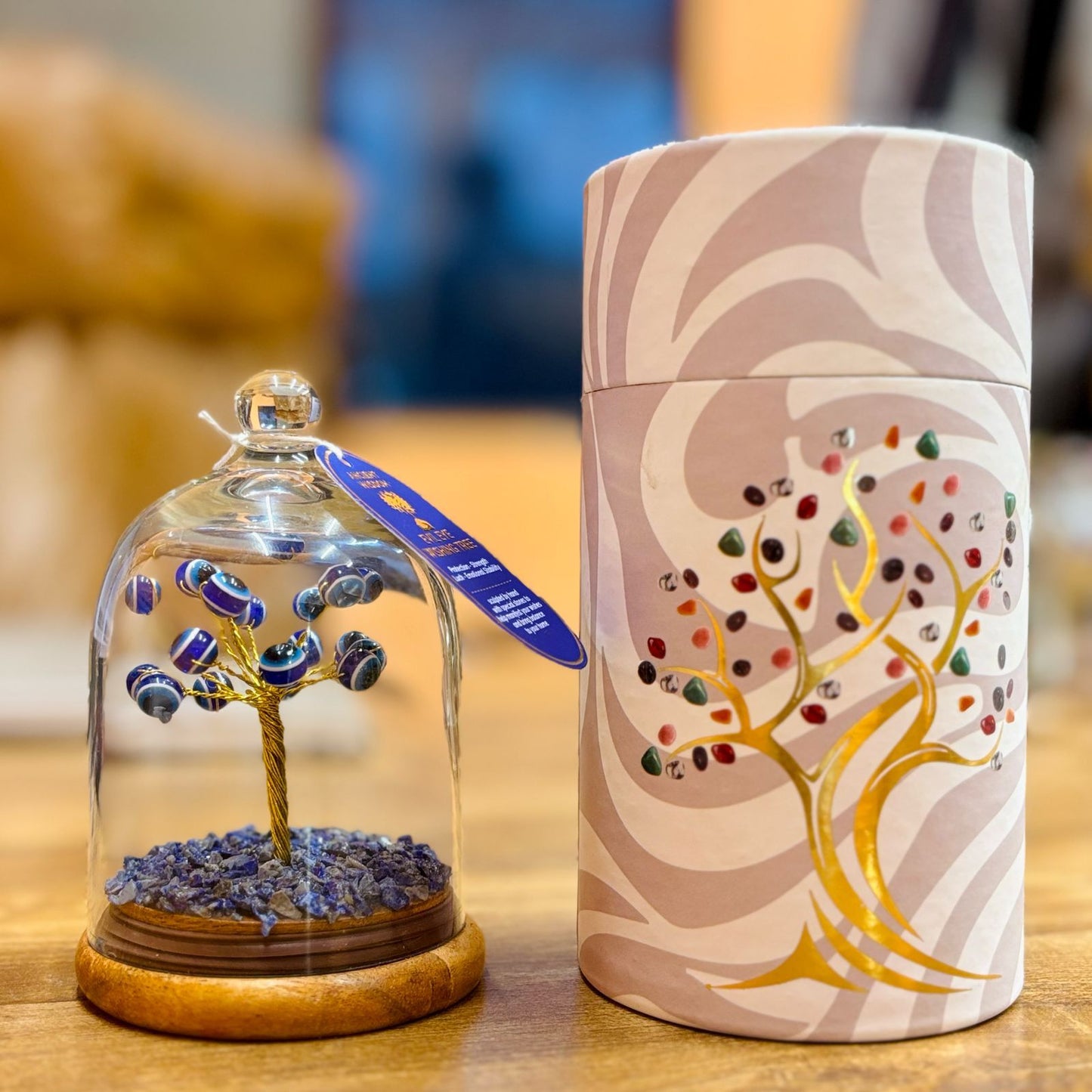 Decorative item with a tree inside a glass dome and a cylindrical container with artistic design on a wooden surface.