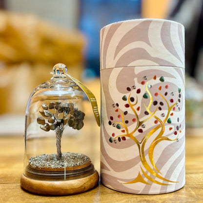 Decorative item with a tree inside a glass dome and a cylindrical container with tree design on a wooden surface.