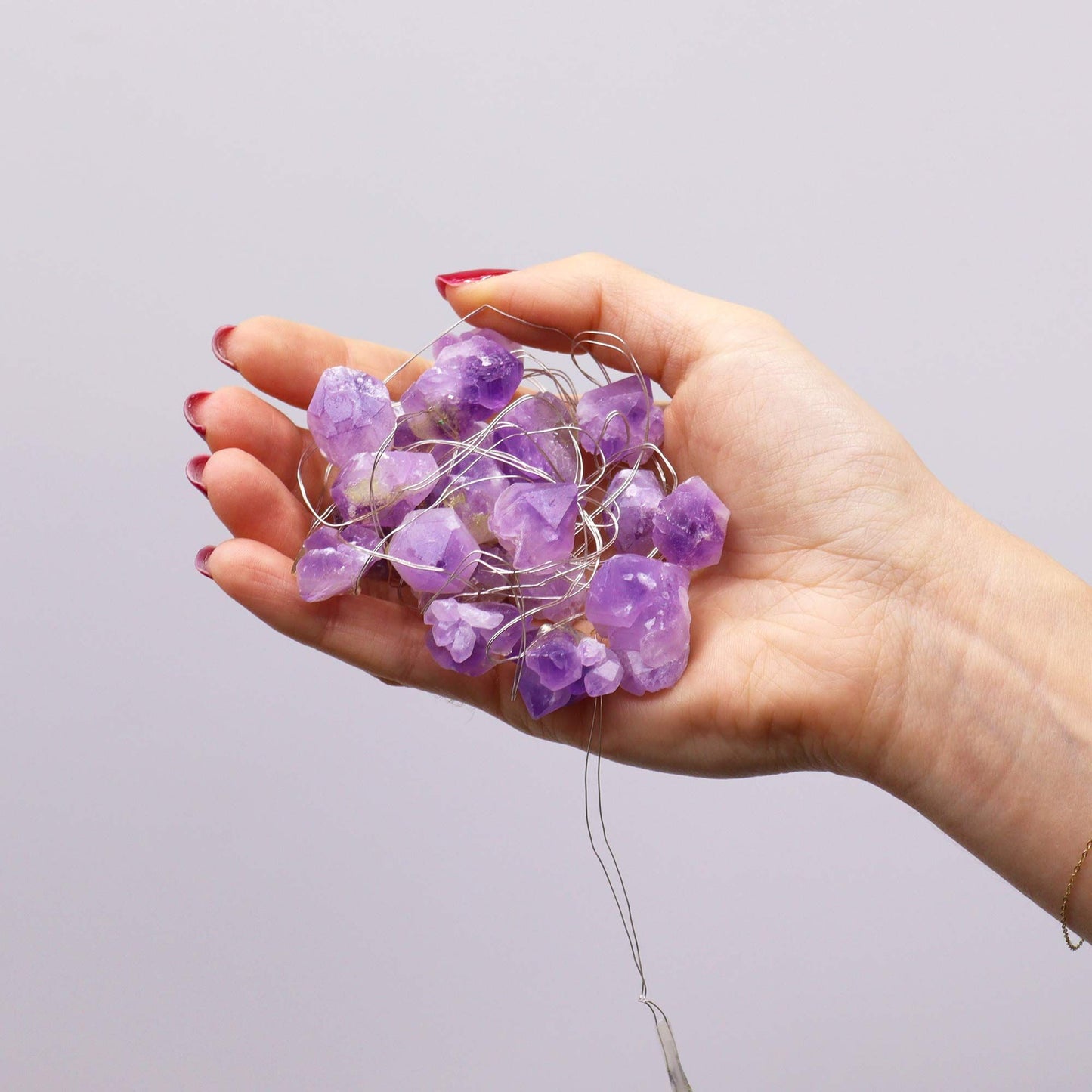 Hand holding a string of purple crystal beads against a plain background