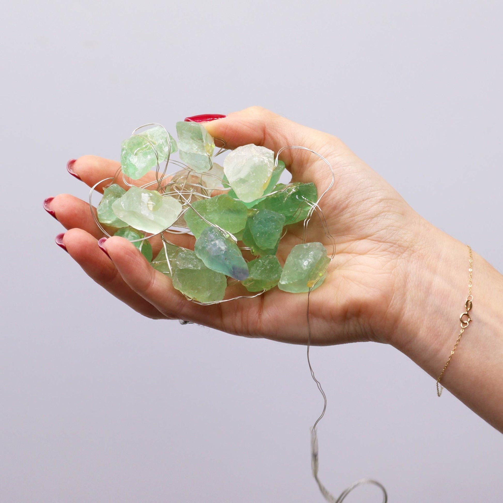 Hand holding a string of green sea glass against a plain background