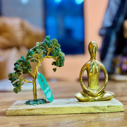 Decorative figure of a gold statue and green tree on a wooden base with a blurred background.