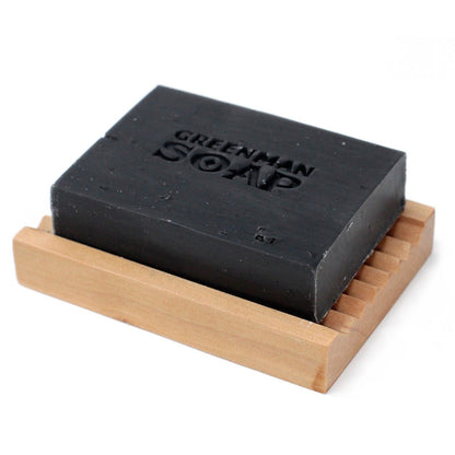Black soap bar on a wooden soap dish with 'Greenman Soap' branding.