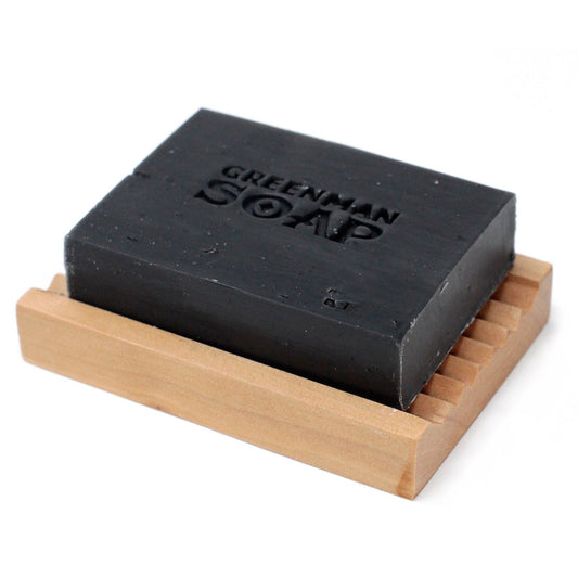 Black soap bar on a wooden soap dish with 'Greenman Soap' branding.