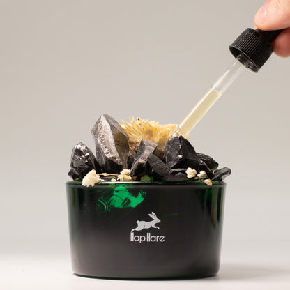 Black container with crystals and a dropper, featuring a brand logo on a gray background