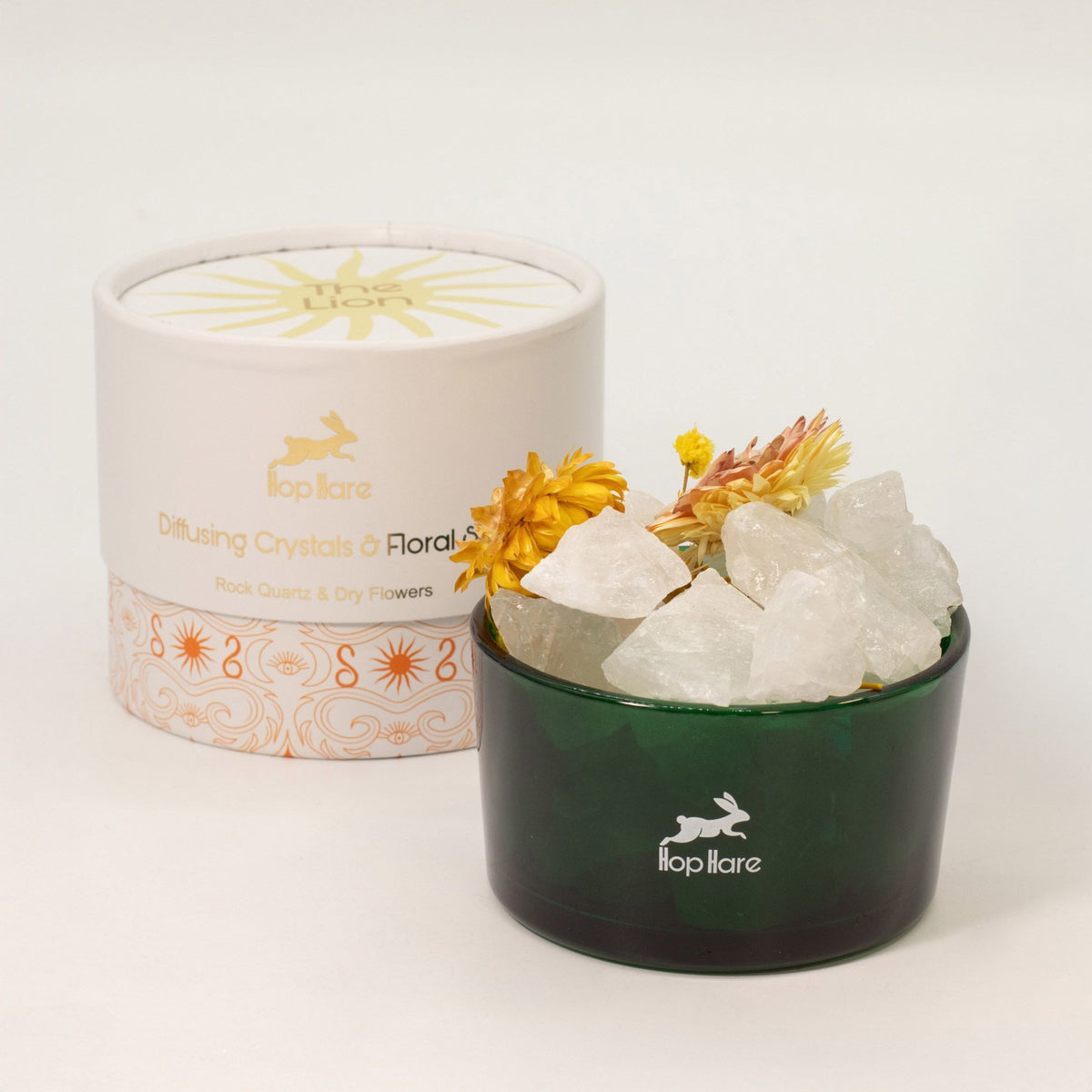 Green container with white crystals and yellow flowers next to a branded white lid on a light background