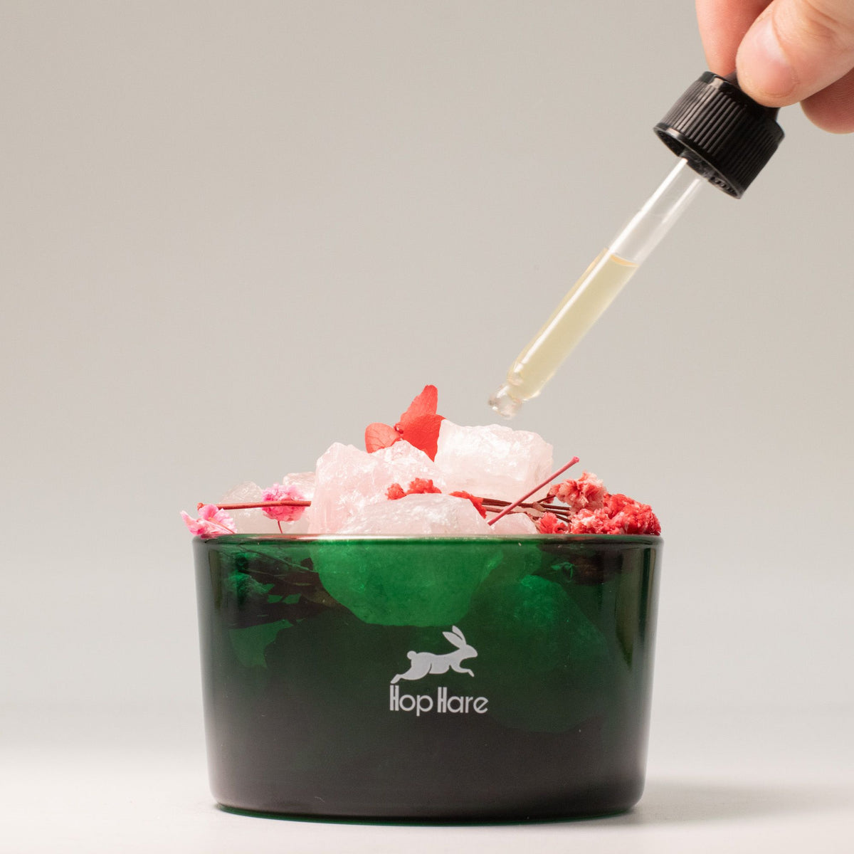 Green container with ice and red flowers, dropper adding liquid, brand 'flop hare' visible