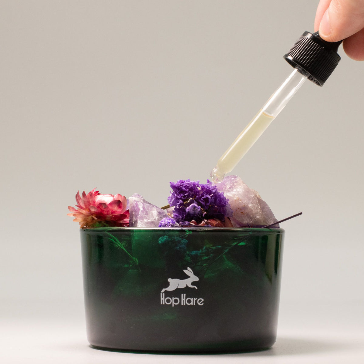 Lip balm container with flowers and a dropper adding liquid.