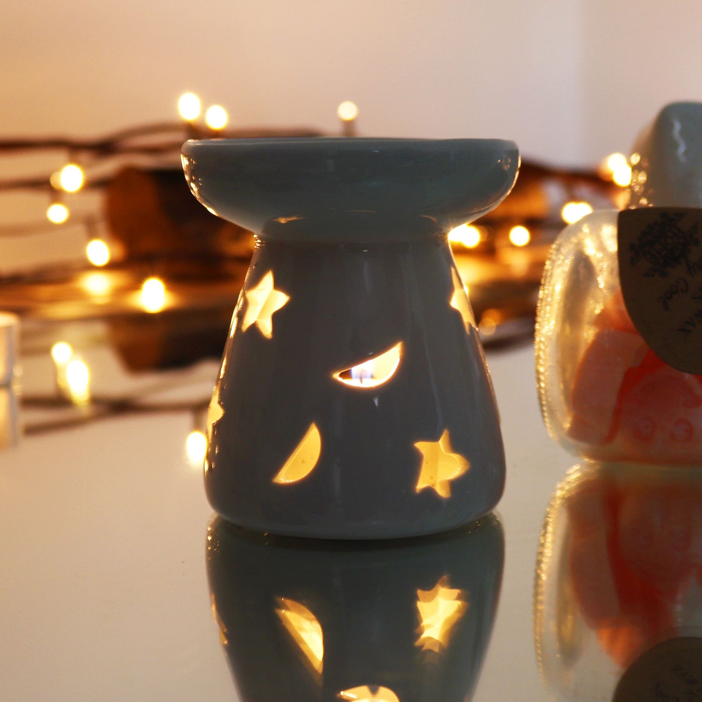 Decorative tealight holder with star cutouts on a reflective surface with blurred lights in the background