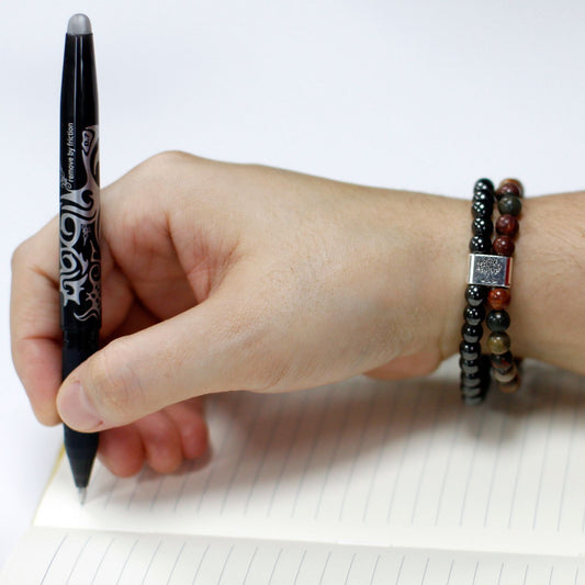 Hand holding a pen over a notebook with a bracelet on a white background