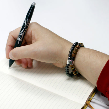 Hand holding a pen over a notebook with a bracelet on a white background