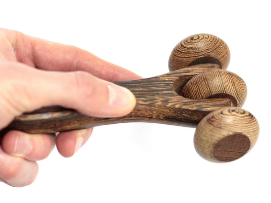 Wooden hand massager held by a hand on a white background