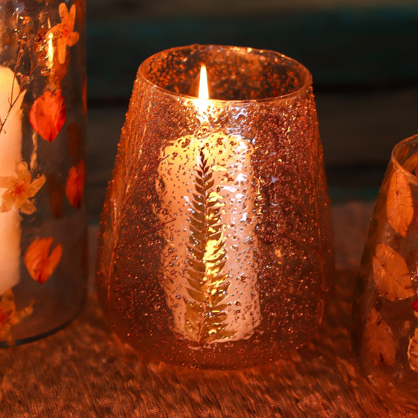 Decorative candle in a textured glass holder with a warm glow on a dark background.