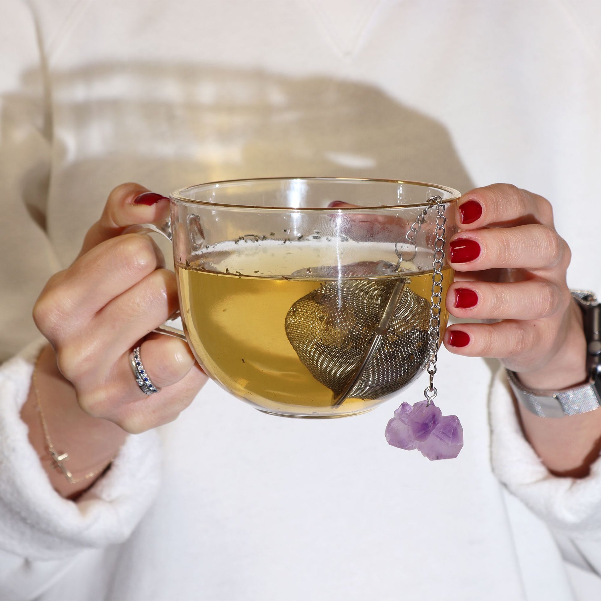 Person holding a glass mug of tea with a decorative teabag holder.
