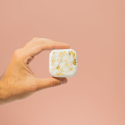 Hand holding a small white container with gold flakes against a beige background