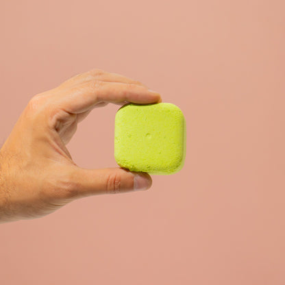 Hand holding a green shower steamer against a beige background