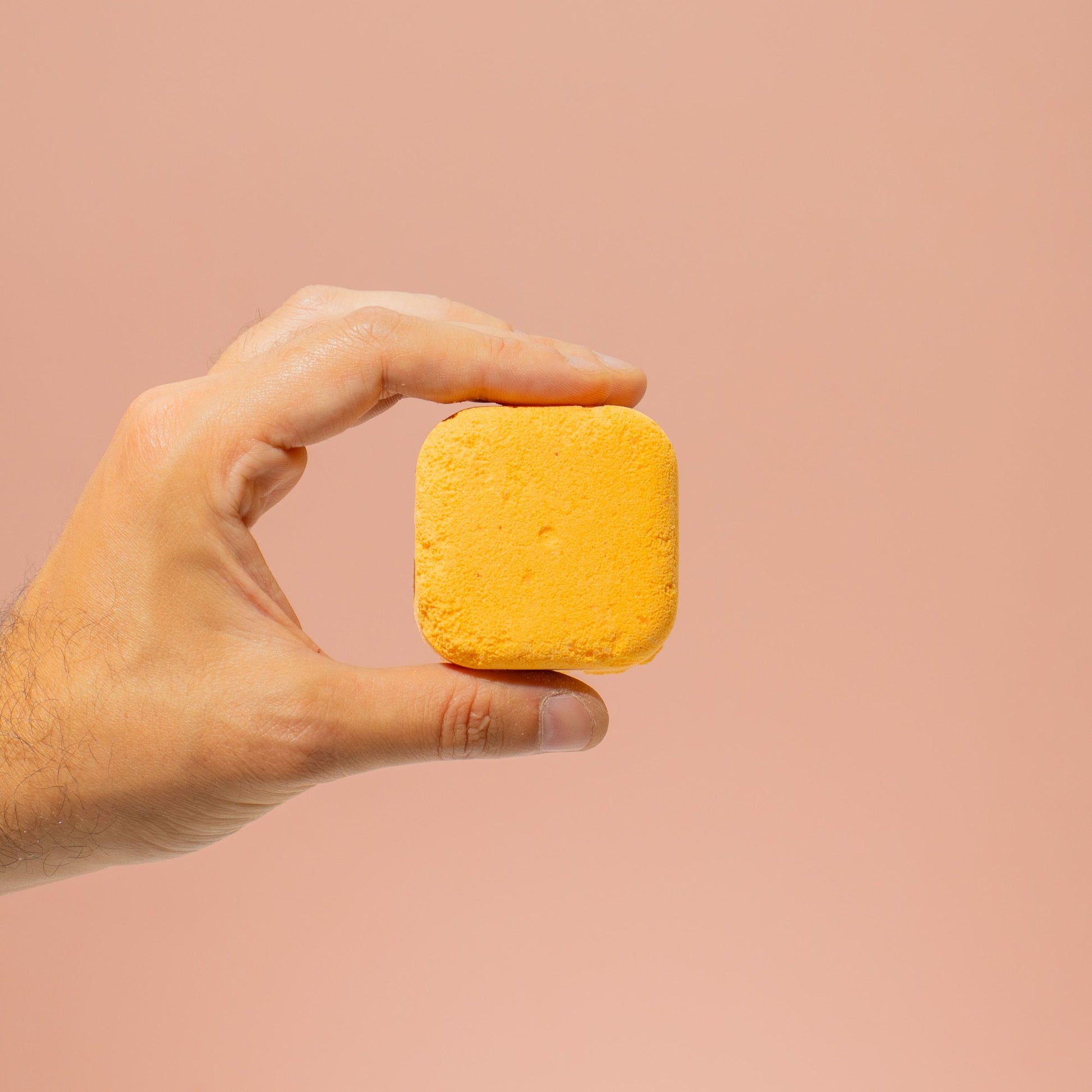Hand holding a yellow bar of soap against a beige background